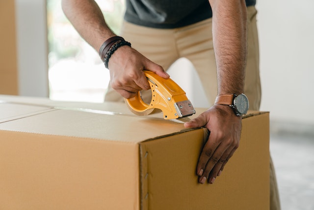 person using a tape role close a moving box